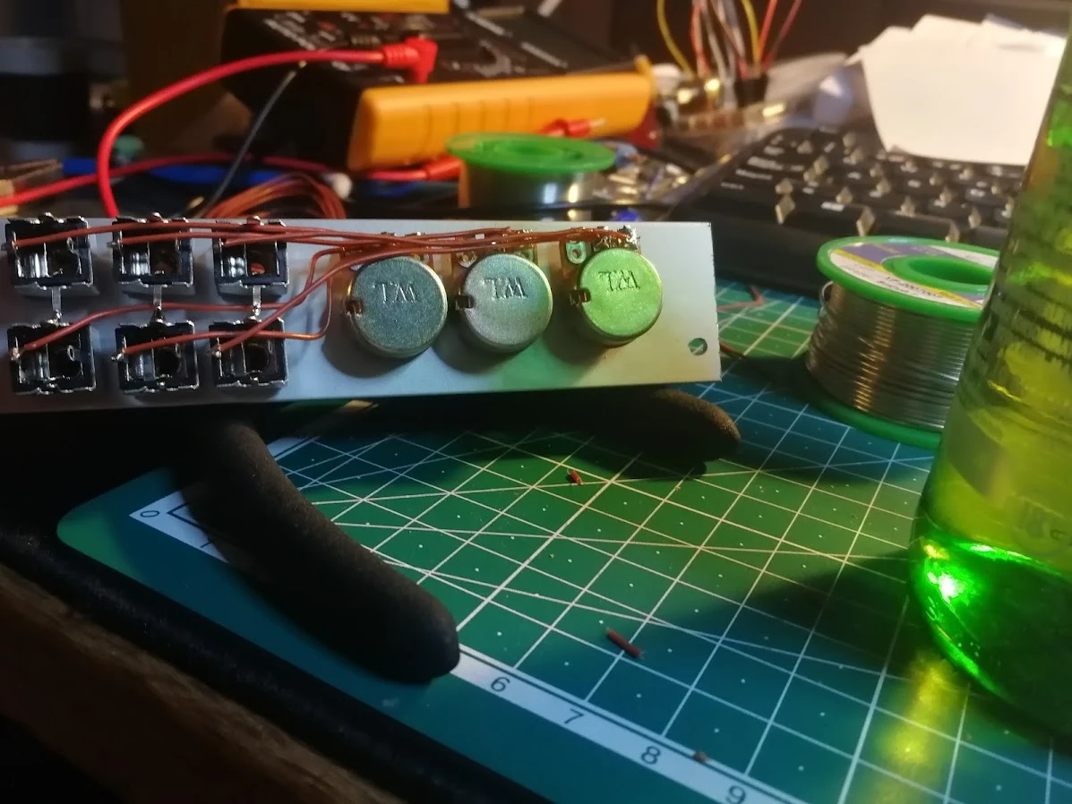 A hand-wired electronics panel on a workbench beside a green drink