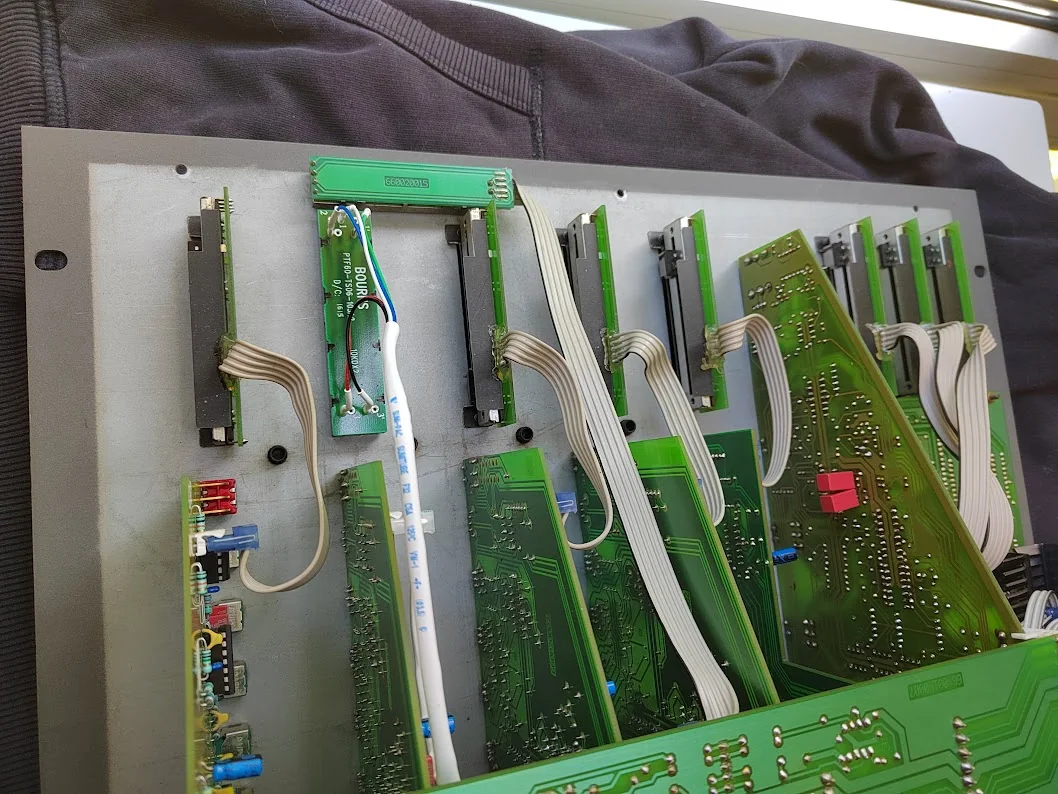 Inside the open Rodec mixer, showing upright channel boards, ribbon cables, and faders mounted behind the front panel, including a Bourns unit.