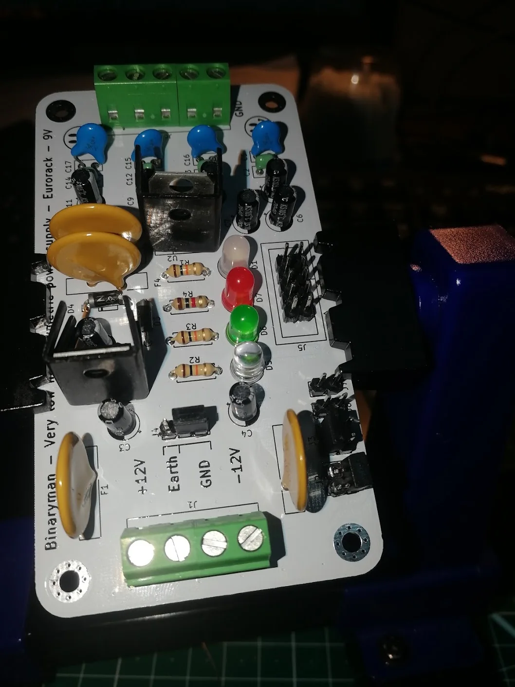 A populated supply card held in a vice, showing screw terminals, heatsinks, capacitors, headers, and LEDs.