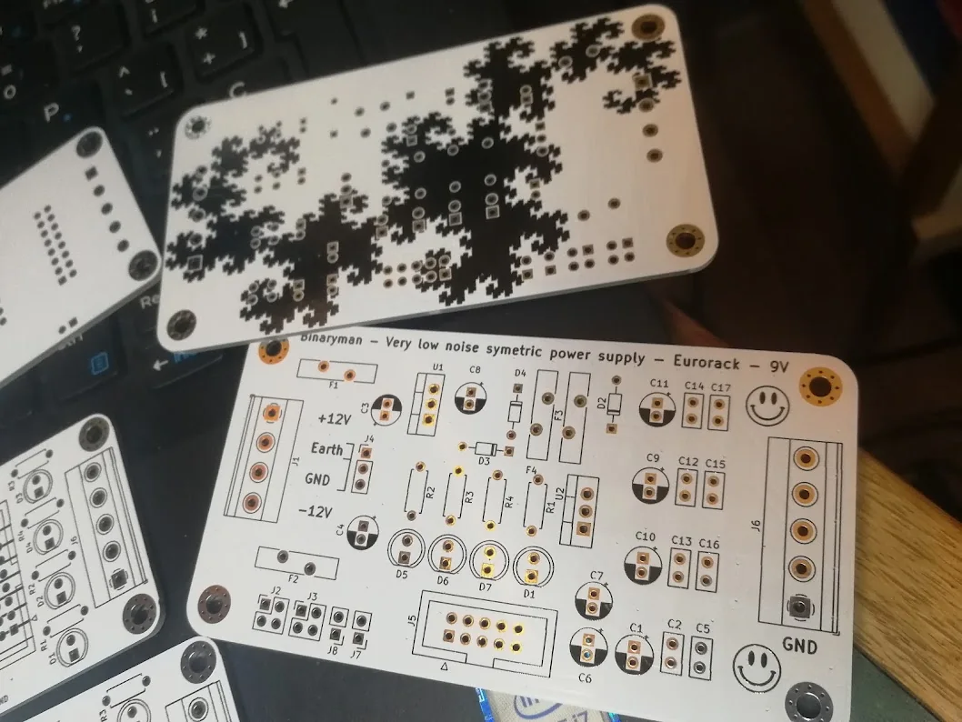 The component side of a supply PCB beside its reverse side with black fractal artwork.